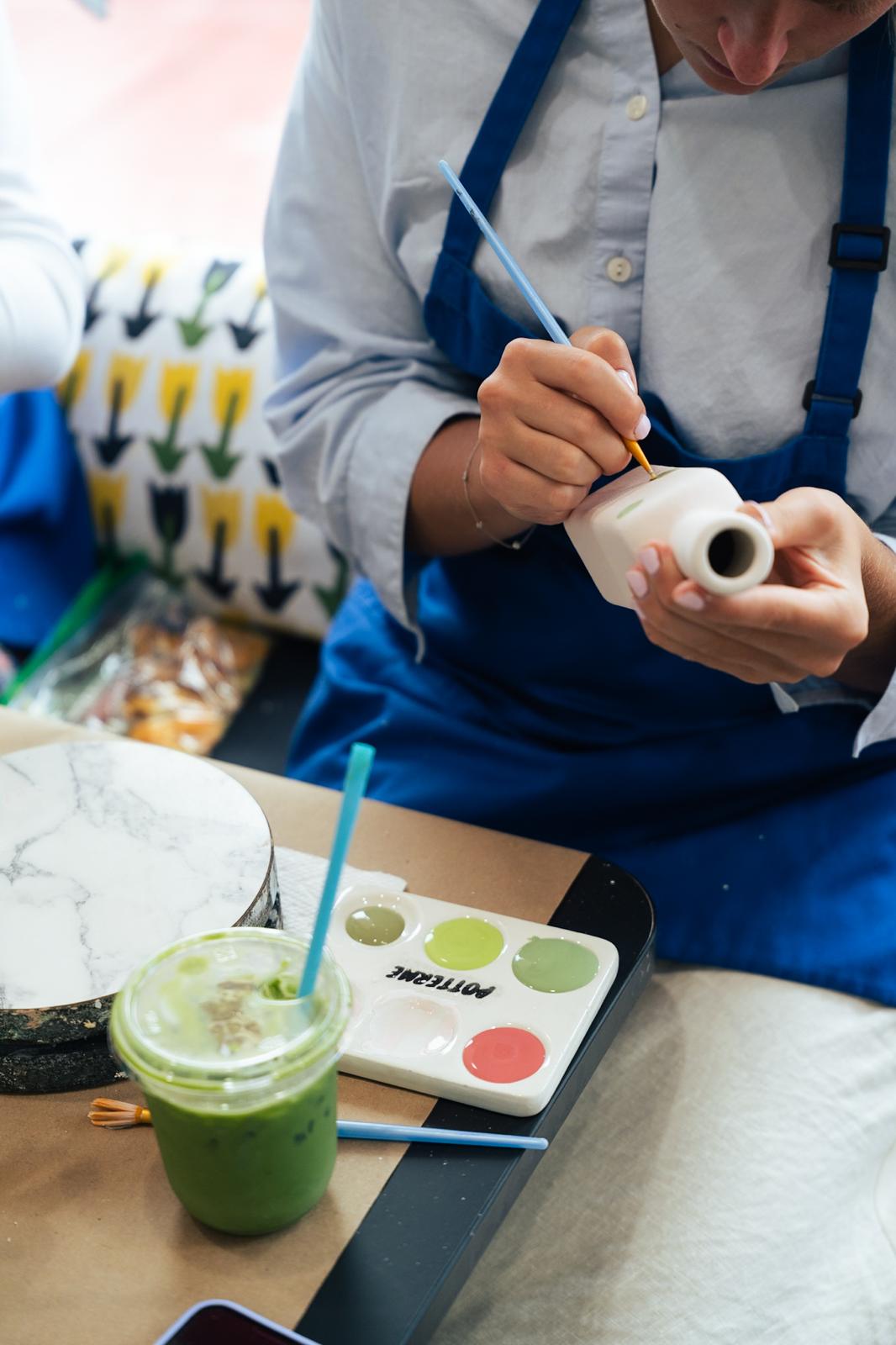 A guest in a blue apron painting a small ceramic vase