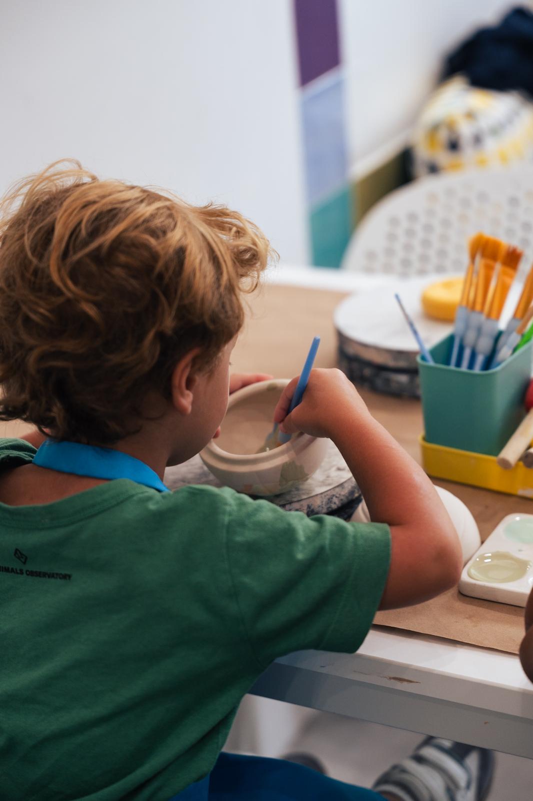 A child carefully painting the inside of a ceramic bowl at PotterMe
