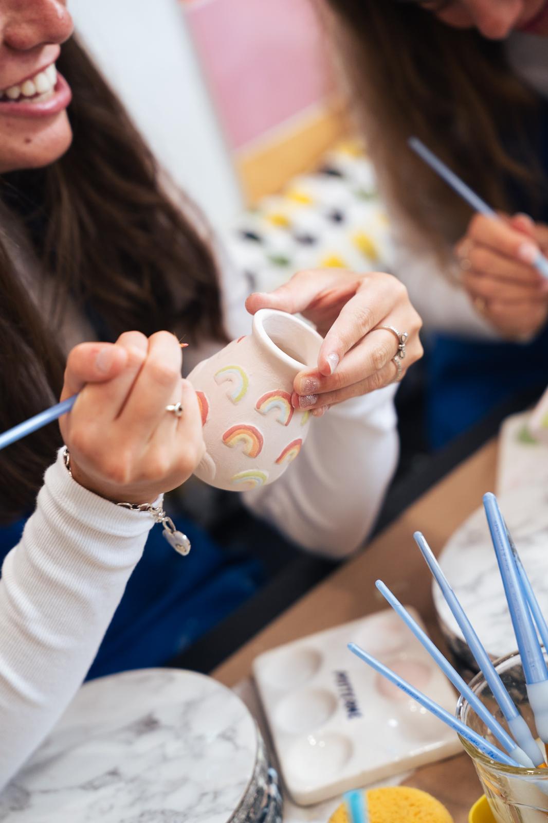 A smiling guest painting rainbow shapes on a ceramic piece at PotterMe